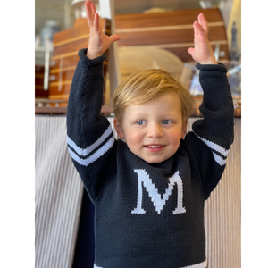 Child wearing the varsity sweater with a navy base color and a light blue "M" monogram and stripes.